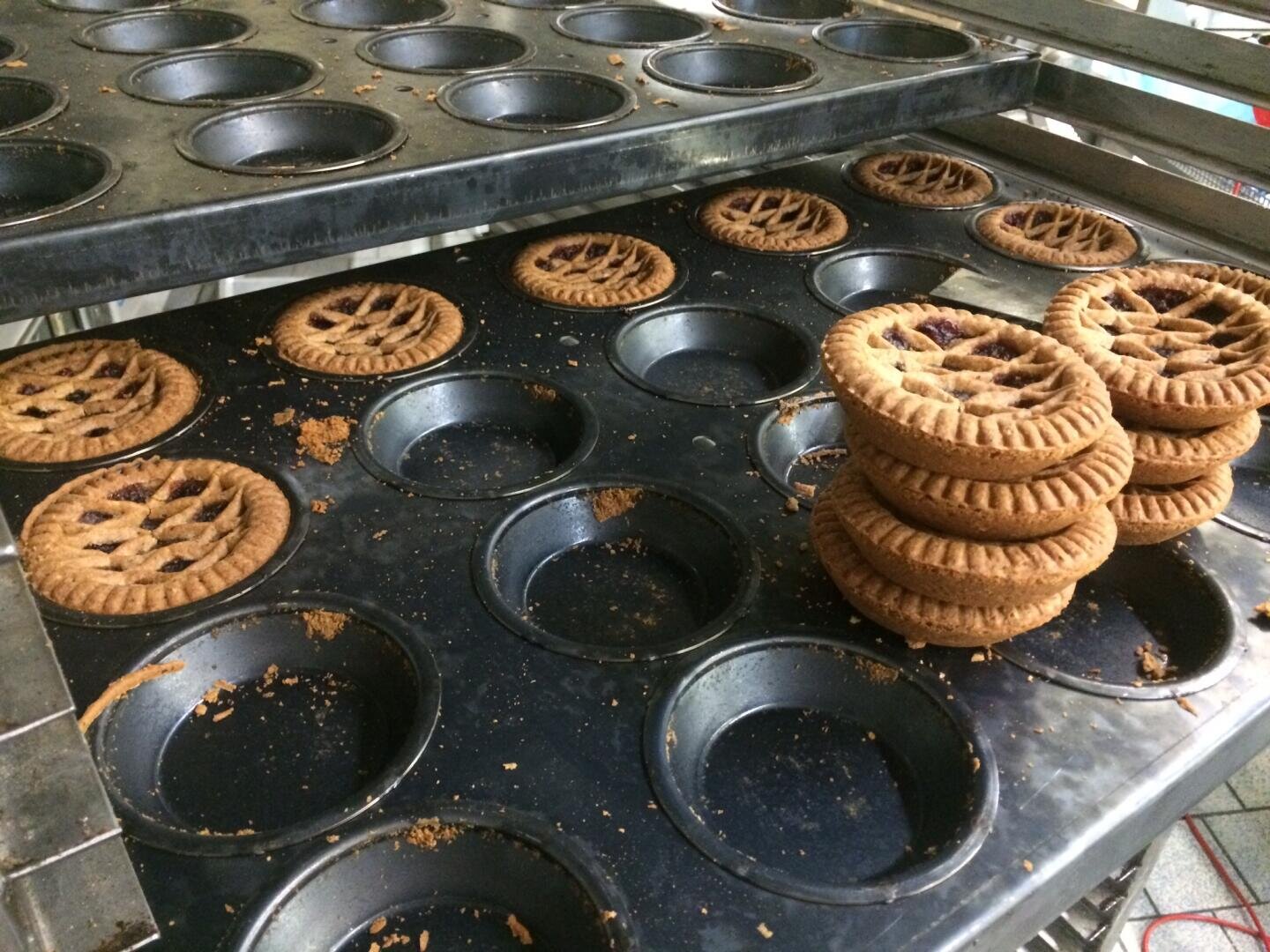 Frisch gebackene Törtchen in Muffinformen auf Metallgittern, wobei mehrere Törtchen in zwei Stapeln aufgeschichtet sind und Krümel um die Formen herum verstreut liegen.