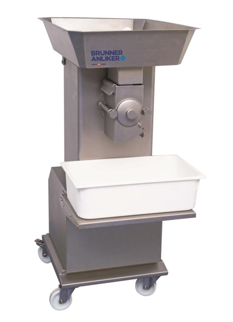 Eine industrielle Lebensmittelverarbeitungsmaschine aus Edelstahl mit großem Einfülltrichter der Marke Brunner Anliker steht auf Rollen. Auf einem Regal unterhalb der Maschine steht ein weißer Kunststoffbehälter.