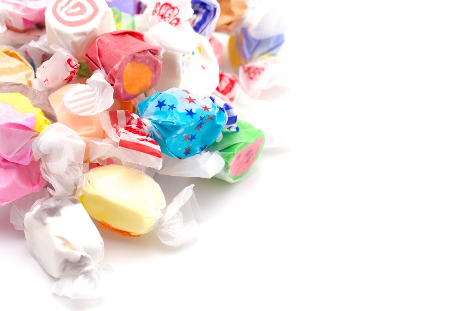 Ein Stapel bunter Salzwasser-Taffy-Bonbons, in Wachspapier eingewickelt, auf einem weißen Hintergrund angeordnet, mit etwas Freiraum auf der rechten Seite.