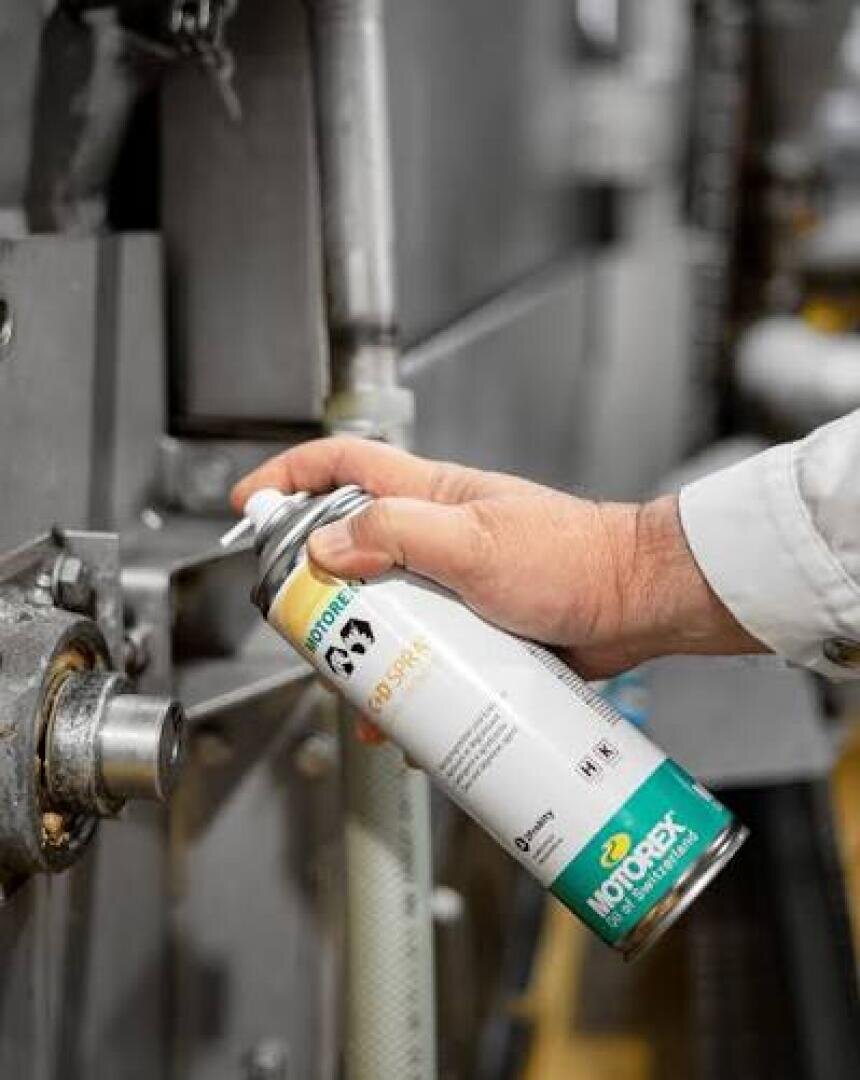 Eine Person hält eine Dose „WD-40 Specialist Machine & Engine Degreaser“ in der Hand und sprüht den Entfetter auf ein Metallteil einer Industriemaschine.