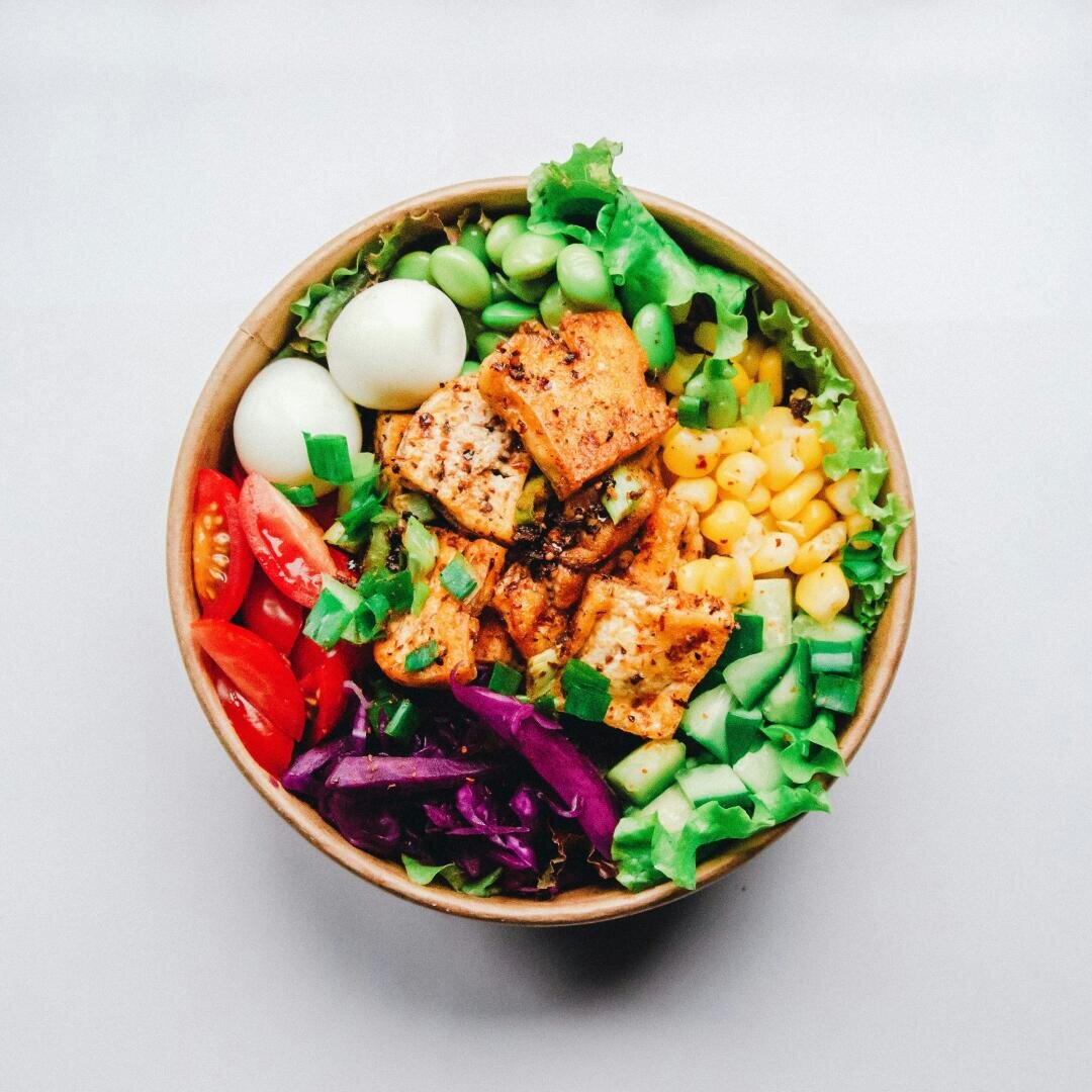 Eine Schüssel Salat mit Tofu, Edamame, Mais, Rotkohl, Tomaten, Gurke, Salat und zwei hartgekochten Eiern.