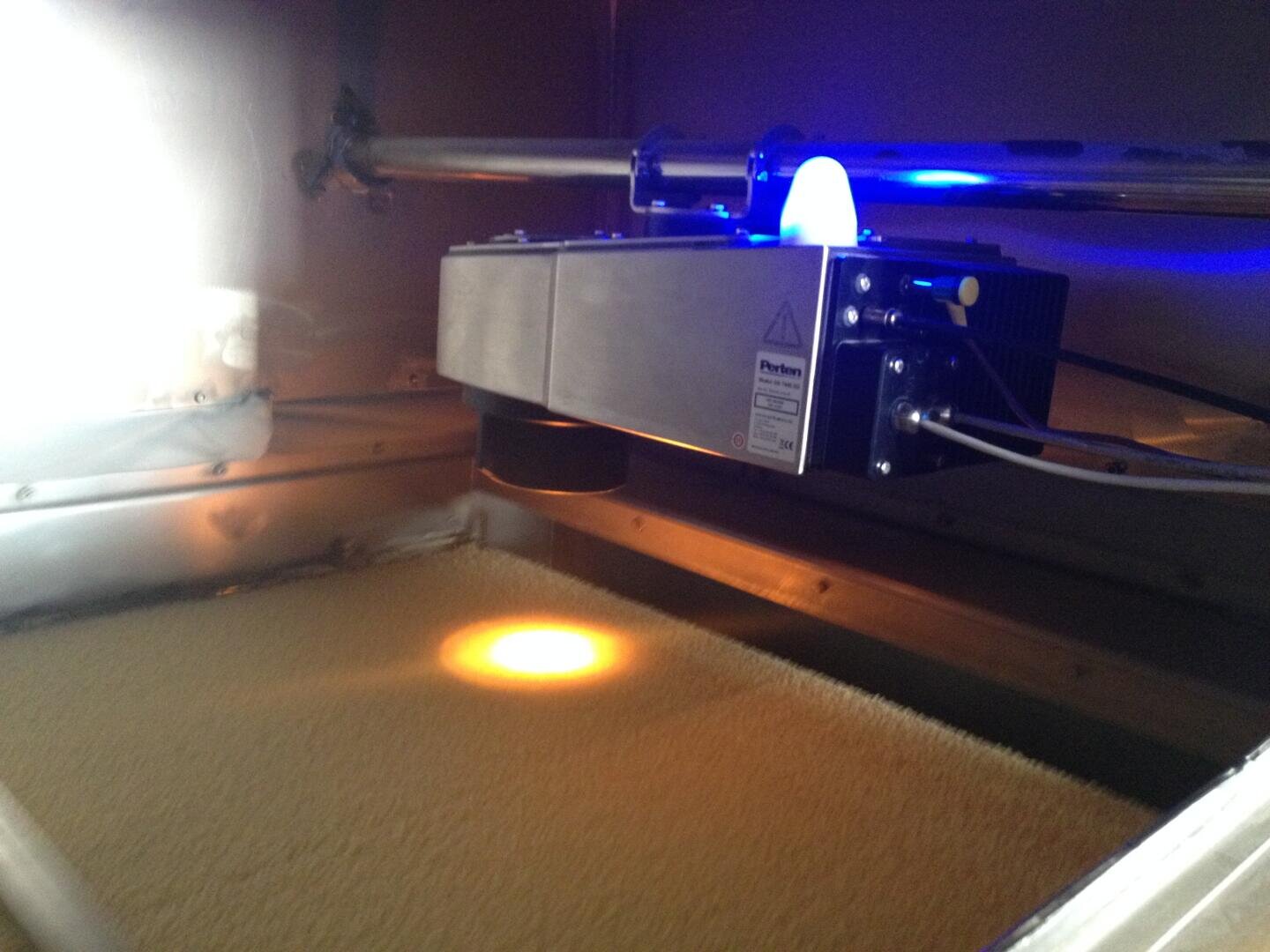 Eine Nahaufnahme eines 3D-Druckers im Einsatz, der mithilfe eines Lasers Pulvermaterial in einer geschlossenen Kammer zu einer festen Schicht verschmilzt.
