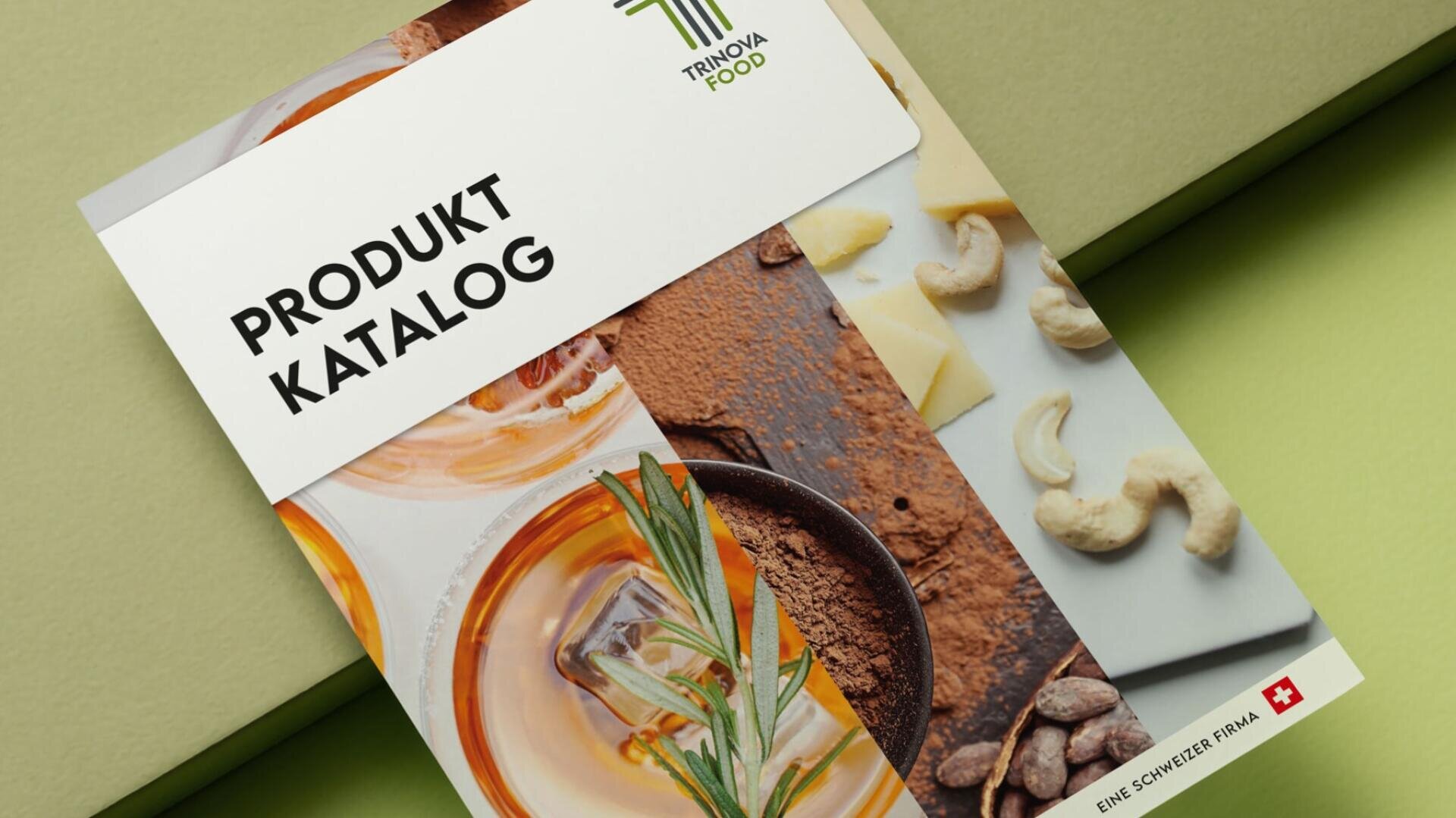 Nahaufnahme eines Produktkatalogs von Trinova Food, auf dessen Titelseite Bilder von Rosmarin, Gewürzen, Cashewnüssen, Käse und Kakao zu sehen sind, mit einem Symbol der Schweizer Flagge in der unteren rechten Ecke.