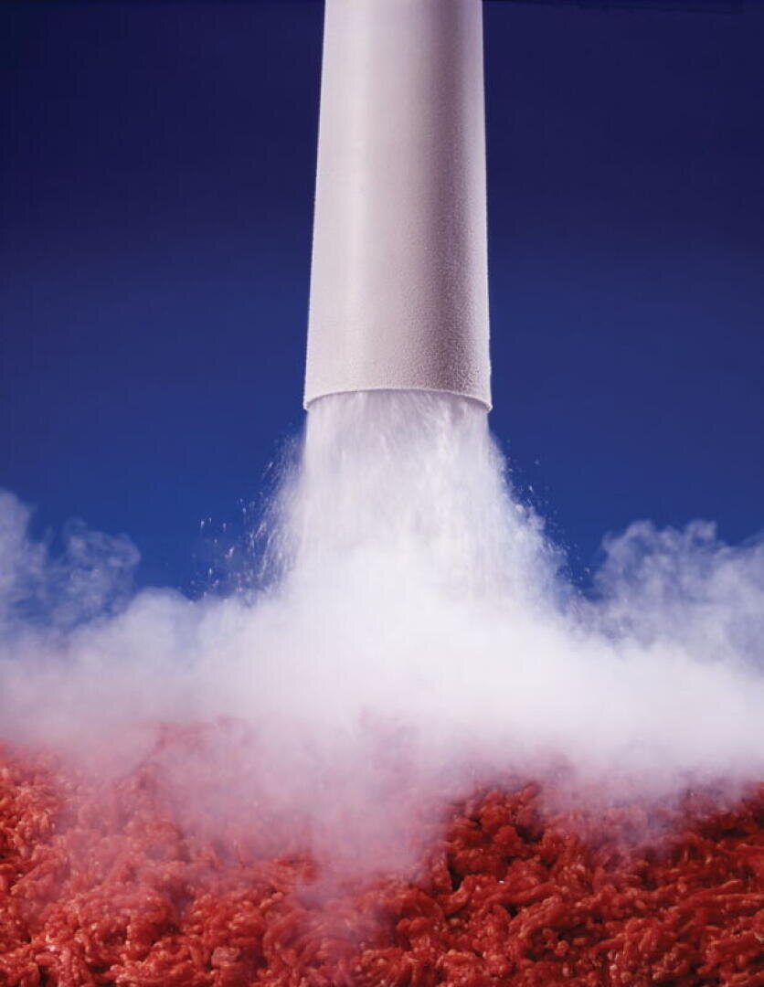 Aus einem weißen Rohr strömt eine Dampf- oder Gaswolke auf einen Haufen rohes Hackfleisch vor blauem Hintergrund.