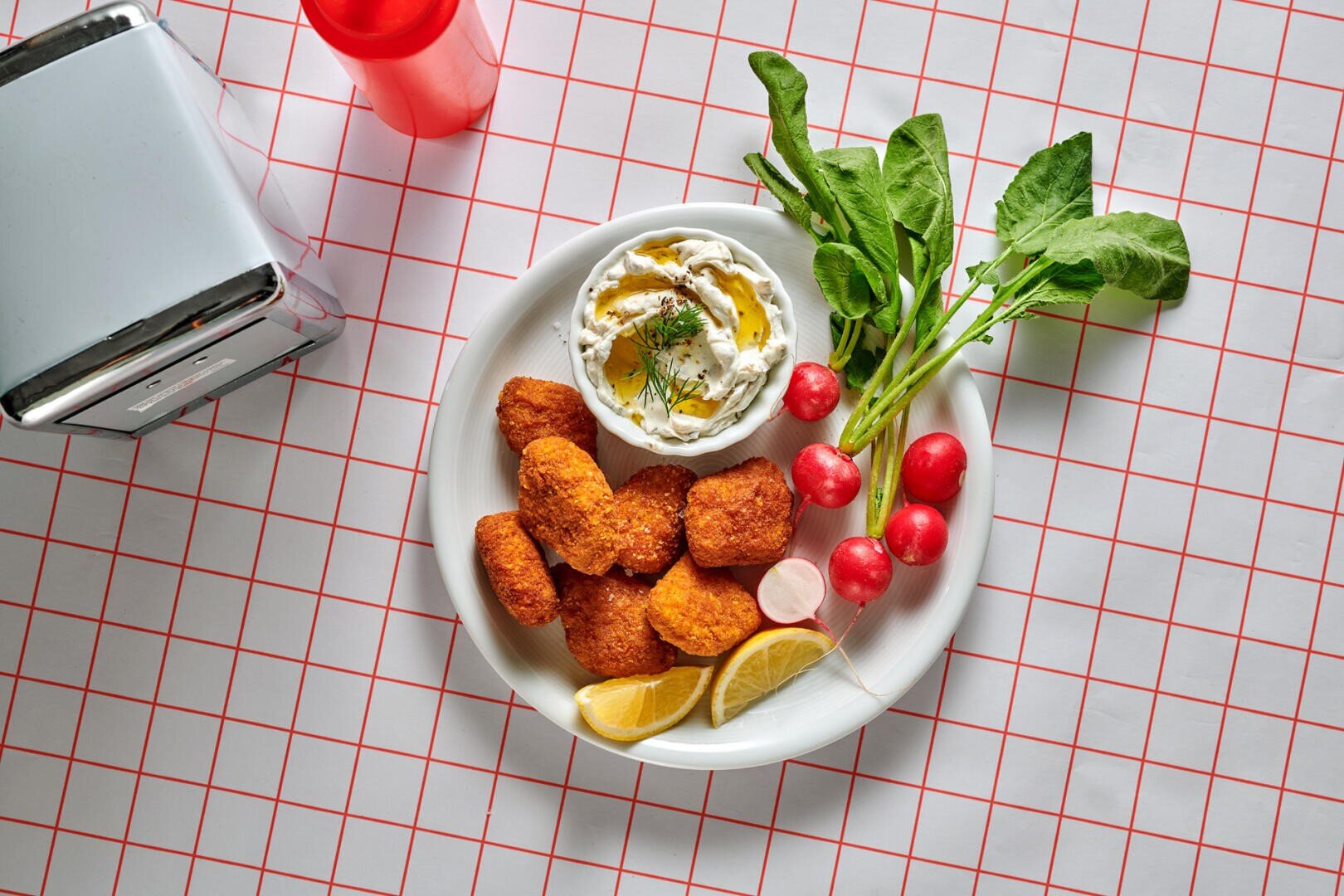Ein Teller mit frittierten Nuggets, serviert mit einer Schüssel Dip, frischen Radieschen und Zitronenschnitzen.