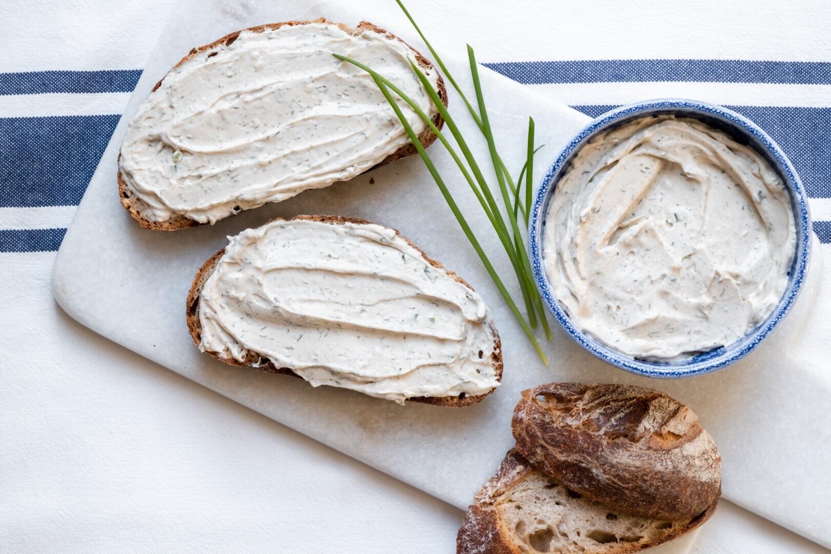 Zwei Scheiben Brot und eine kleine Schüssel mit Kräuter-Frischkäse, garniert mit frischem Schnittlauch.