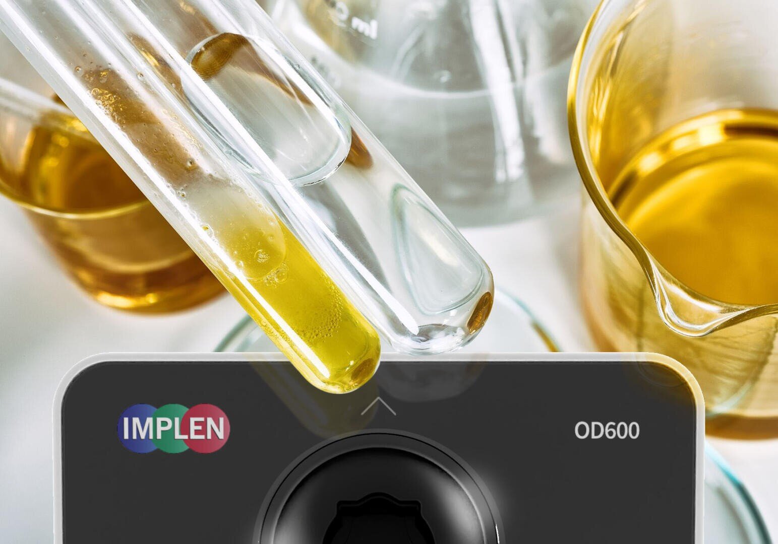 Zwei mit gelber Flüssigkeit gefüllte Glasreagenzgläser, die über einem Implen OD600-Spektralphotometer positioniert sind.