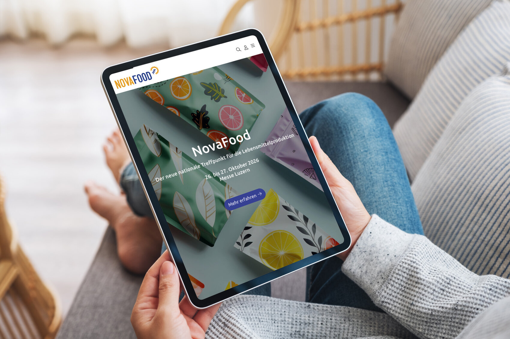Eine Person hält ein Tablet mit der NovaFood-Website in der Hand, auf der bunte Illustrationen von Früchten und Veranstaltungshinweise für die Lebensmittelmesse in Lausanne, Schweiz, vom 3. bis 5. Oktober 2026 zu sehen sind.